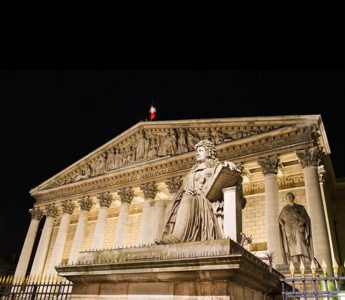 Façade illuminée de nuit de l'Assemblée nationale, avec la statue de d'Aguesseau au premier plan